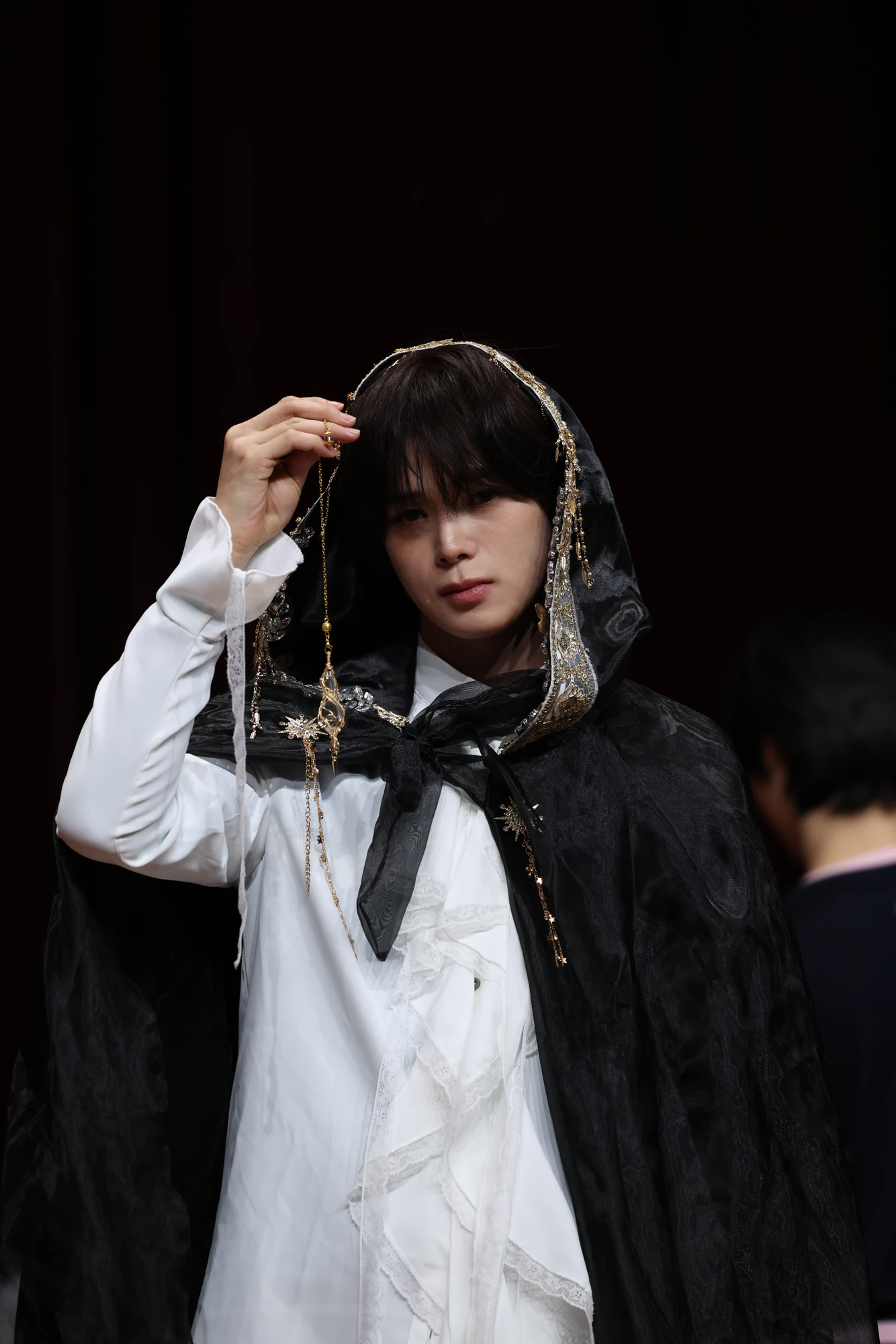 K wearing a dark, dramatic layered outfit.