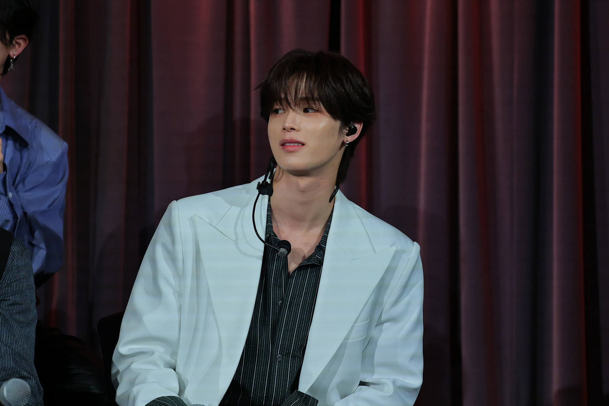 K seated on stage with a microphone.
